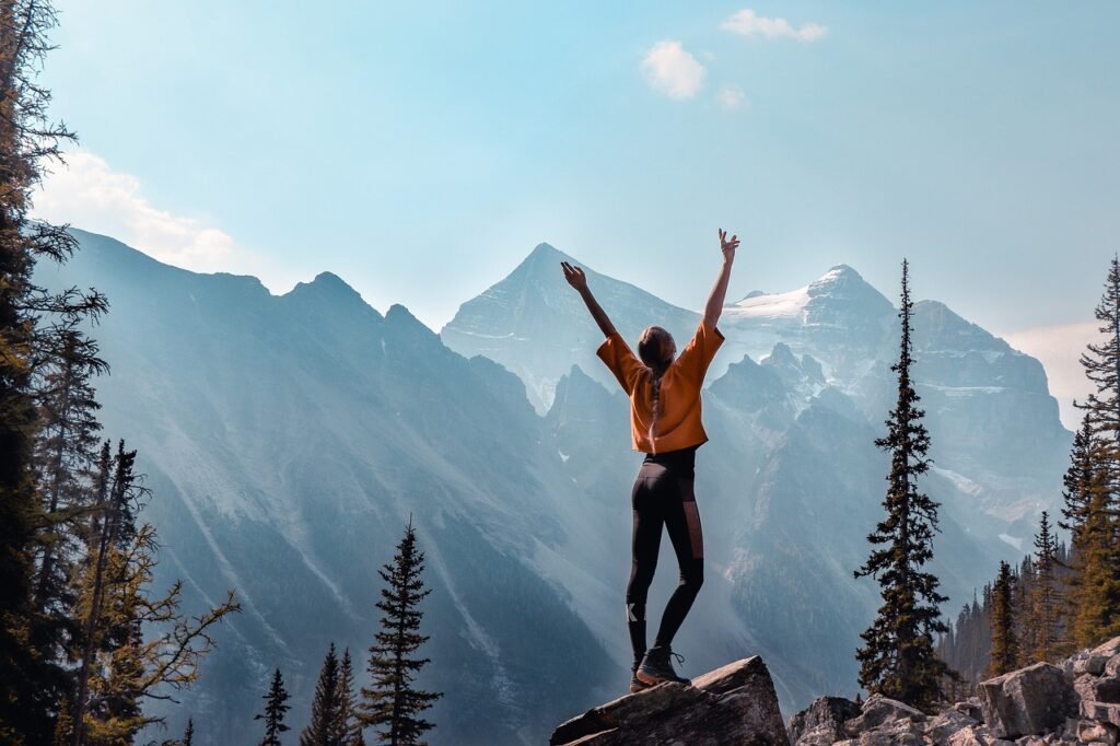 A girl’s back with up-lifting arms on top of the mountains, indicating excitement and relief